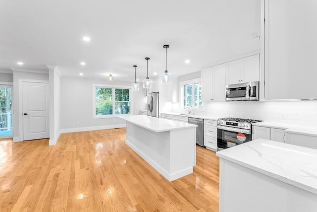 kitchen with white cabinets, hanging light fixtures, appliances with stainless steel finishes, tasteful backsplash, and a kitchen island