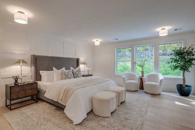 bedroom featuring crown molding, light wood-style floors, visible vents, and a decorative wall