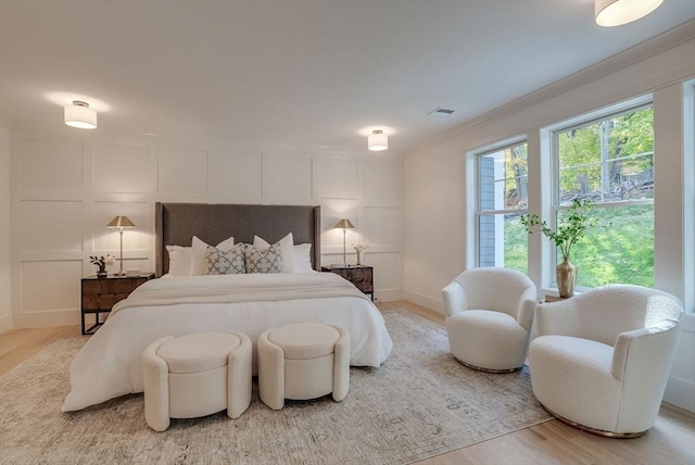 bedroom featuring crown molding, light wood-type flooring, visible vents, and a decorative wall