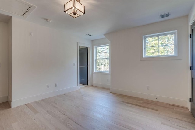 empty room featuring light wood-type flooring, attic access, visible vents, and baseboards