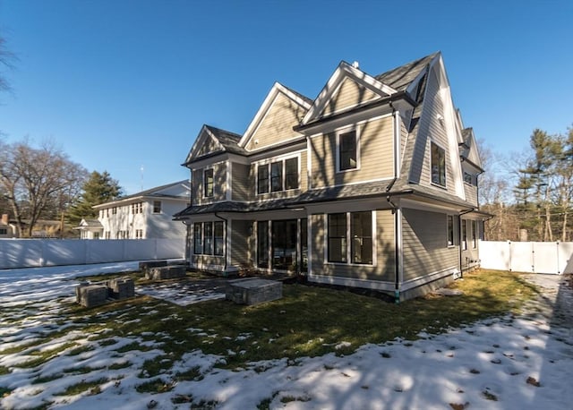 snow covered rear of property featuring a lawn, fence, and a gate