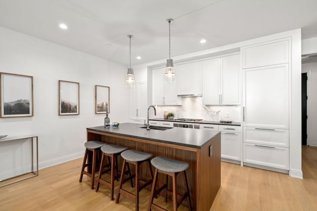 100 Linden St Unit 202, Wellesley, MA 02482 - kitchen featuring dark countertops, light wood-style flooring, a breakfast bar area, a kitchen island with sink, and recessed lighting
