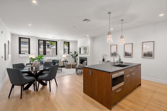 100 Linden St Unit 202, Wellesley, MA 02482 - kitchen featuring dark countertops, brown cabinetry, an island with sink, modern cabinets, and light wood-type flooring