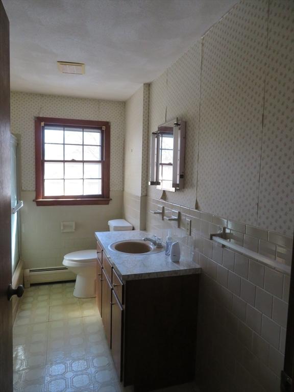 full bathroom featuring baseboard heating, a healthy amount of sunlight, and wallpapered walls