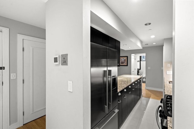 kitchen with baseboards, high quality fridge, dark cabinets, light stone countertops, and recessed lighting