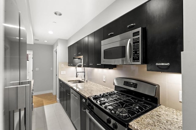 kitchen with tasteful backsplash, baseboards, dark cabinets, stainless steel appliances, and a sink