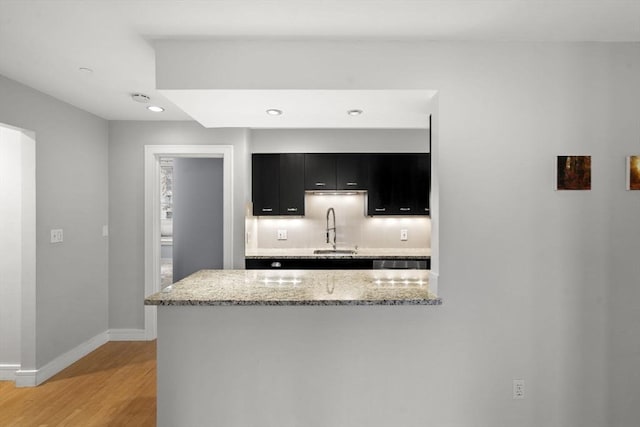 kitchen with light stone counters, light wood-style flooring, a sink, dark cabinetry, and baseboards