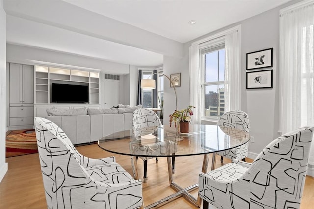 dining space with baseboards, light wood-type flooring, visible vents, and a healthy amount of sunlight