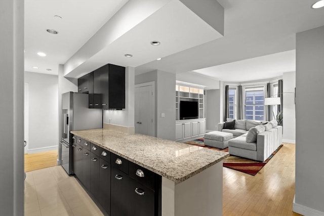 kitchen featuring freestanding refrigerator, dark cabinetry, light wood-style flooring, and baseboards