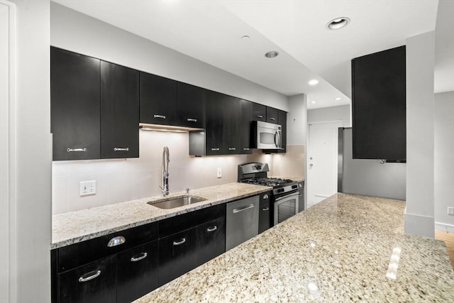 kitchen featuring light stone counters, recessed lighting, a sink, dark cabinetry, and appliances with stainless steel finishes