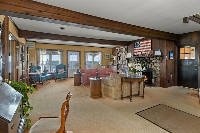 carpeted living room featuring beam ceiling, a stone fireplace, and wood walls