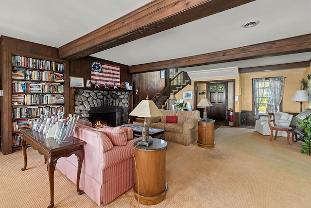 sitting room with beamed ceiling, a stone fireplace, and wood walls