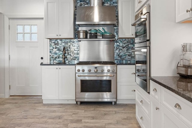 kitchen with tasteful backsplash, white cabinetry, dark stone counters, and high end range