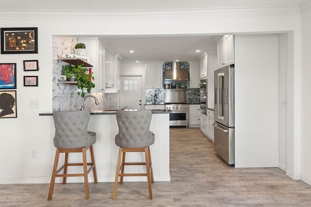 kitchen featuring white cabinets, decorative backsplash, wall chimney exhaust hood, kitchen peninsula, and stainless steel appliances