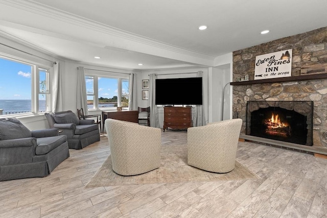 living room with a stone fireplace, a water view, light hardwood / wood-style floors, and ornamental molding