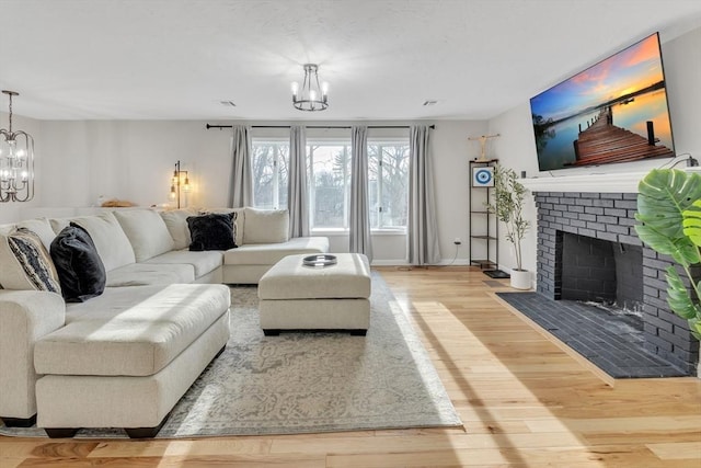 living room featuring an inviting chandelier, a brick fireplace, and wood-type flooring