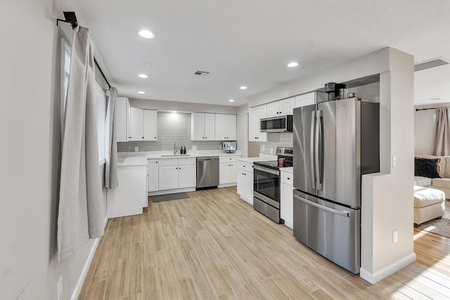 kitchen featuring sink, white cabinets, decorative backsplash, stainless steel appliances, and light wood-type flooring