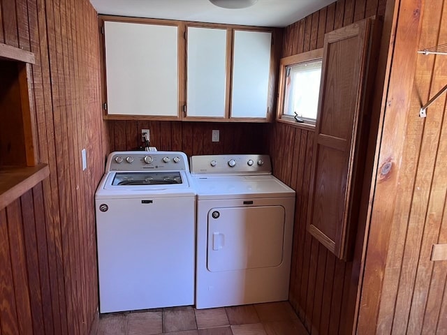 clothes washing area with cabinets, wood walls, and separate washer and dryer