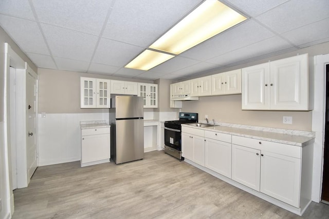 kitchen featuring appliances with stainless steel finishes, light wood-type flooring, a drop ceiling, sink, and white cabinets