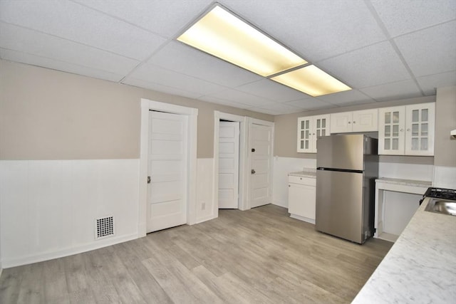 kitchen with white cabinets, light wood-type flooring, a paneled ceiling, and stainless steel refrigerator