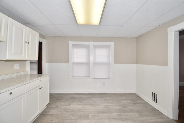 unfurnished dining area with a paneled ceiling and light wood-type flooring