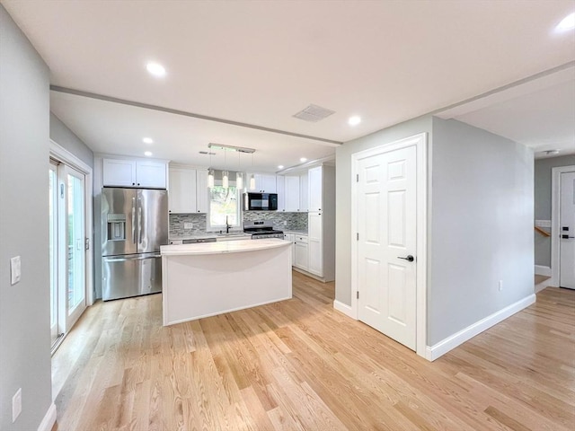 kitchen with light wood-type flooring, appliances with stainless steel finishes, decorative backsplash, and white cabinetry