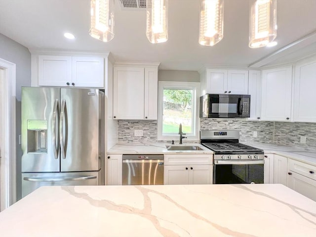 kitchen with a sink, light stone counters, white cabinetry, appliances with stainless steel finishes, and decorative backsplash