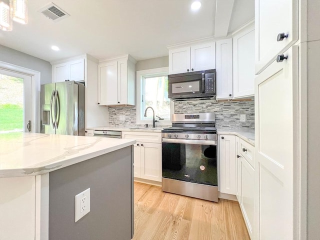 kitchen featuring visible vents, a sink, white cabinets, light wood-style floors, and appliances with stainless steel finishes