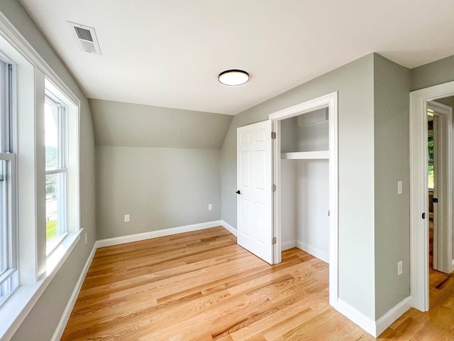 unfurnished bedroom with light wood-type flooring, visible vents, a closet, baseboards, and vaulted ceiling