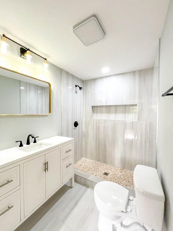 bathroom with a tile shower, toilet, and vanity