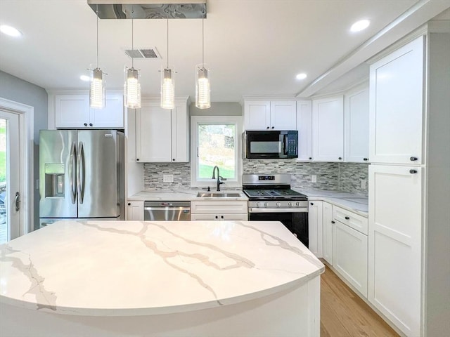 kitchen with a sink, decorative backsplash, white cabinets, appliances with stainless steel finishes, and a center island