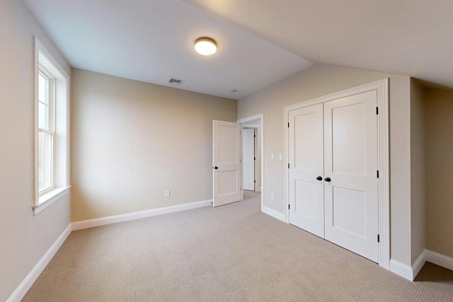 unfurnished bedroom with multiple windows, a closet, light colored carpet, and lofted ceiling