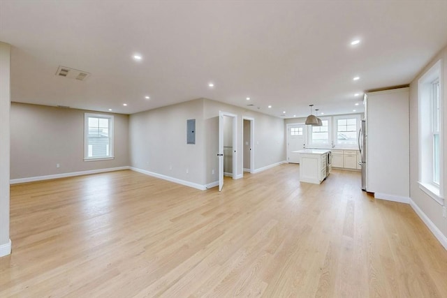 unfurnished living room featuring electric panel, plenty of natural light, and light hardwood / wood-style floors