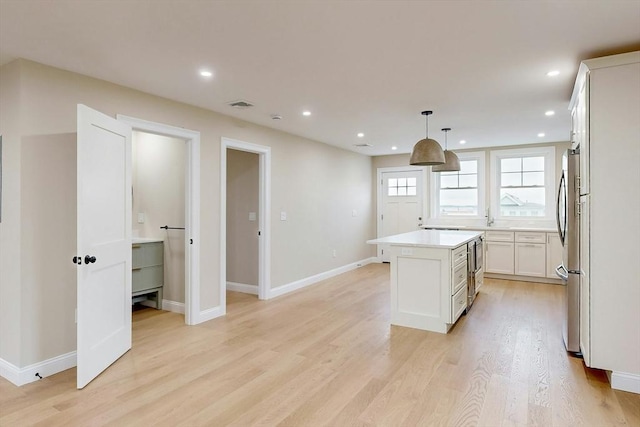 kitchen featuring stainless steel fridge, decorative light fixtures, light hardwood / wood-style flooring, a center island, and white cabinetry