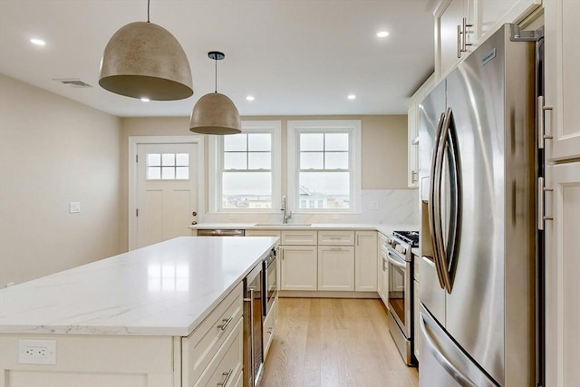 kitchen with pendant lighting, white cabinets, sink, light stone countertops, and stainless steel appliances