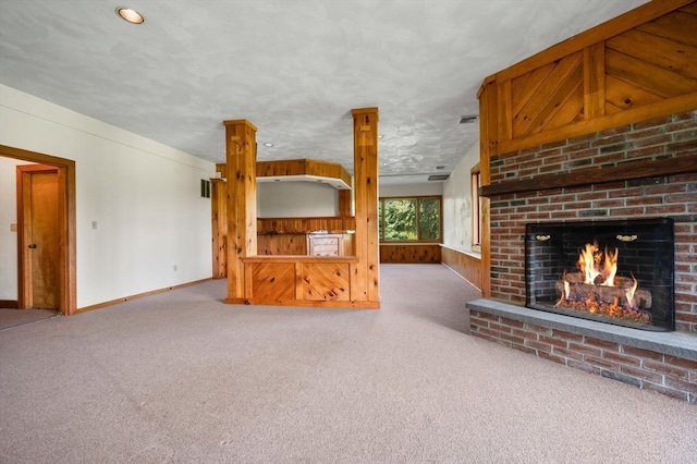 unfurnished living room featuring a fireplace, wood walls, carpet, and a textured ceiling