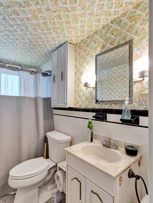 bathroom with toilet, vanity, wallpapered walls, a wainscoted wall, and tile walls