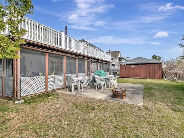 view of green lawn with an outdoor fire pit, a sunroom, a patio area, and an outbuilding
