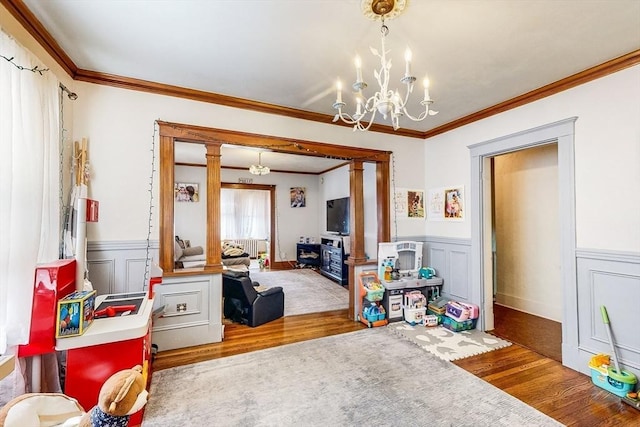 game room with a chandelier, wood finished floors, a wainscoted wall, and crown molding