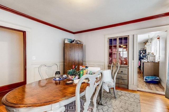 dining space featuring wood finished floors, a wainscoted wall, and ornamental molding