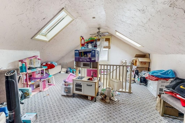 rec room featuring lofted ceiling with skylight, a ceiling fan, a textured ceiling, and carpet floors