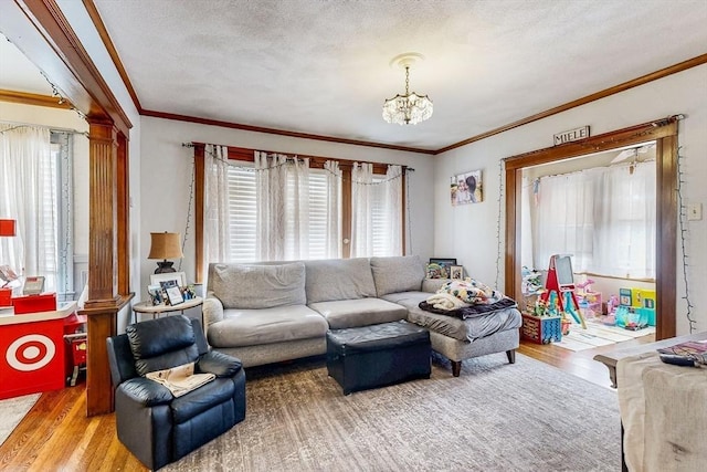 living area featuring ornate columns, wood finished floors, crown molding, and a chandelier