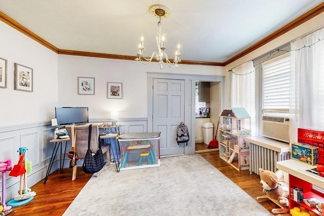 rec room with wood finished floors, cooling unit, a wainscoted wall, a notable chandelier, and crown molding