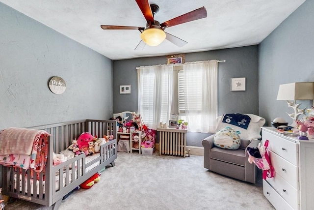 carpeted bedroom featuring a textured wall, a ceiling fan, and a crib