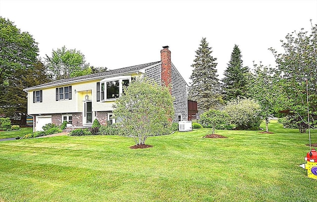 split foyer home featuring a chimney, central AC unit, a front yard, and an attached garage