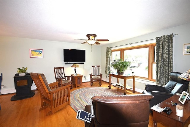 living room with light wood-style flooring, ceiling fan, a wood stove, and baseboards