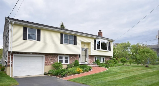 split foyer home featuring a chimney, a front lawn, a garage, driveway, and brick siding