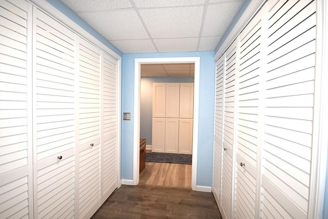 hallway featuring a paneled ceiling, dark wood-style flooring, and baseboards