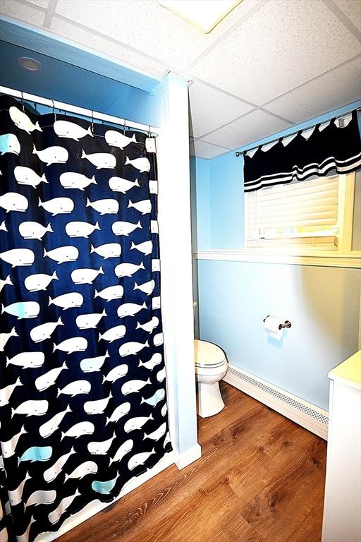 full bath with baseboard heating, wood finished floors, toilet, a paneled ceiling, and curtained shower