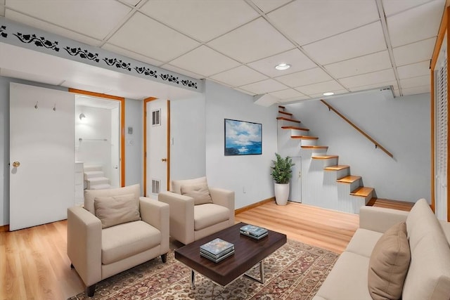 living room featuring wood finished floors, stairs, a drop ceiling, recessed lighting, and baseboards